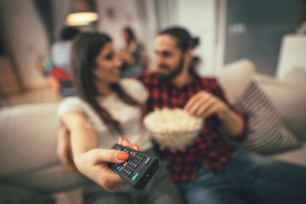 Excited couple is looking movie on TV at home sitting on sofa with popcorn. They have great weekend in nice company indoors.