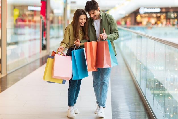 Excited couple looking into shopping bags standing in modern mall