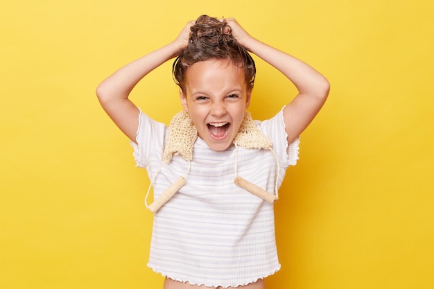 Photo excited crazy little girl with wet hair wearing casual white tshirt standing isolated over yellow background washing hair screaming with widely open mouth