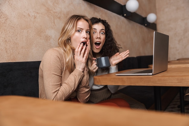 excited emotional shocked girls friends sitting in cafe using laptop computer