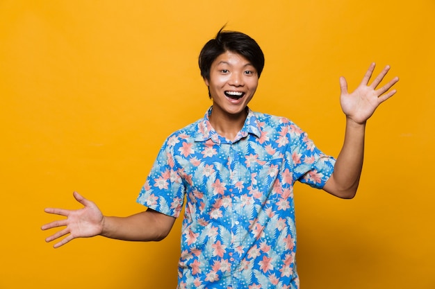 Excited emotional young asian man posing isolated over yellow space.