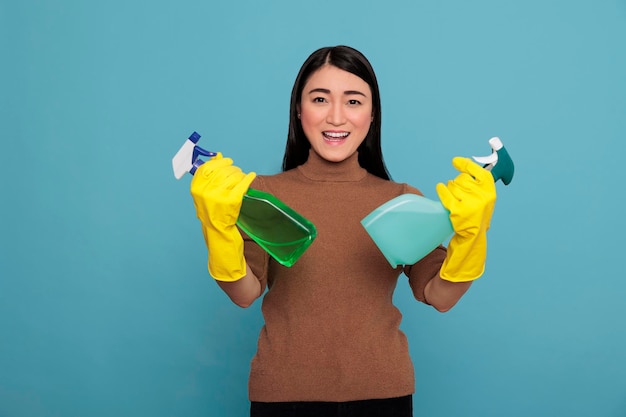 Eccitata donna asiatica energica e sorridente pronta a fare i compiti quotidiani due spray detergente in guanti gialli, concetto di casa di pulizia, ottimista e soddisfatto di uno stato d'animo positivo