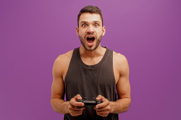 Excited european man play video game on joystick. Young european bearded guy with open mouth. Concept of leisure and entertainment. Isolated on purple background. Studio shoot. Copy space