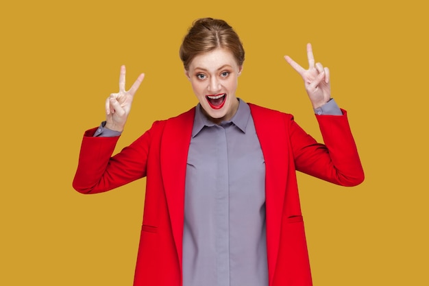 Excited extremely happy woman with red lips showing v sign with both hands celebrating her success