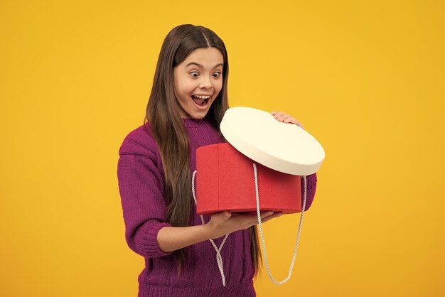 Excited face Child teen girl 1214 years old with gift on yellow isolated background Birthday holiday concept Teenager hold present box Amazed expression cheerful and glad