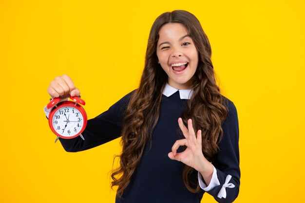 Excited face child teenager girl with alrm clock isolated on yellow background time and deadline concept amazed expression cheerful and glad