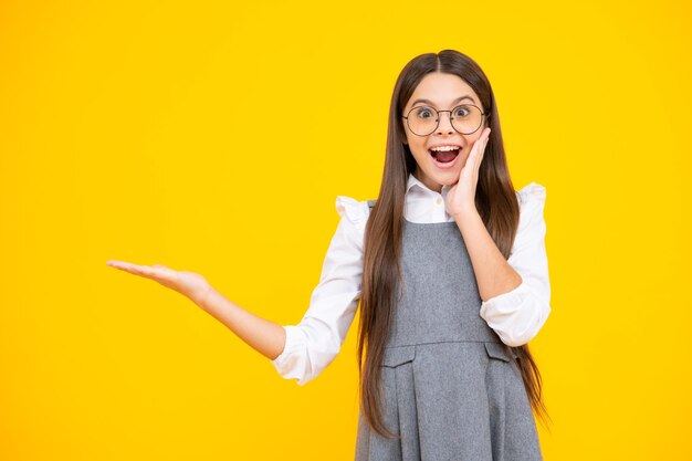 Excited face Look at advert Teenager child points aside shows blank copy space for text promo idea presentation poses against yellow background Amazed expression cheerful and glad