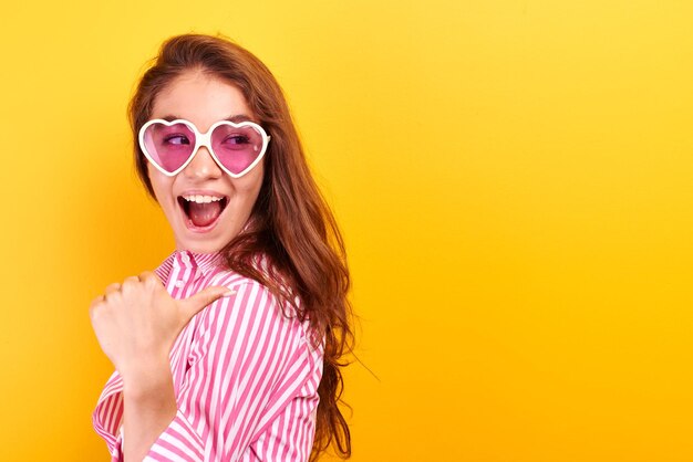 Excited face surprised girl dressed casual isolated in yellow studio. Kazakh woman shows finger on inscription, free copy space for your product