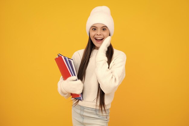 Excited face Winter school Teenager school girl with books in autumn clothes on yellow isolated studio background Amazed expression cheerful and glad