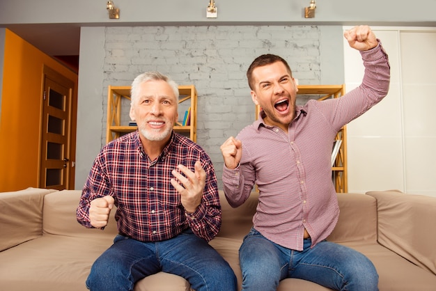 Excited father and son sitting on the sofa and watching football