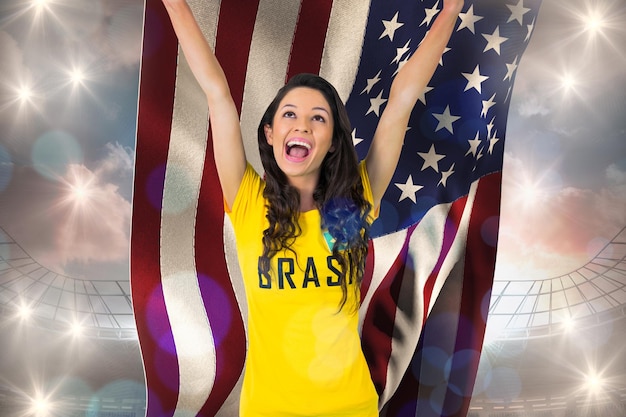 흐린 푸른 하늘 아래 대형 축구 경기장에 대해 미국 국기를 들고 브라질 티셔츠에 흥분된 축구 팬