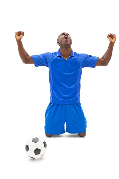 Excited football player in blue cheering on his knees