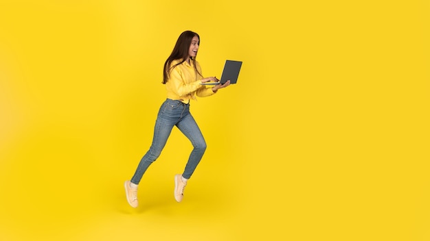 Excited Freelancer Woman Using Laptop Running In Air Yellow Background