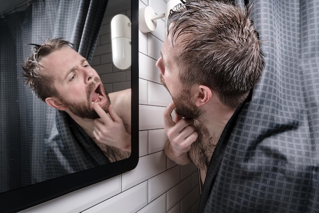 Excited frustrated man opened mouth and carefully examined his teeth in the mirror