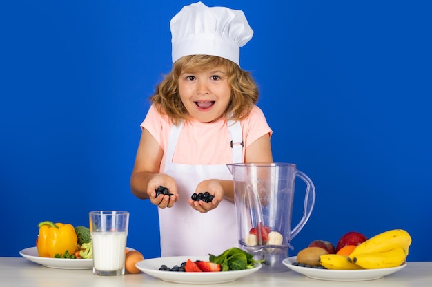 Excited funny chef cook child chef dressed cook baker apron and chef hat cooking blueberries smoothi