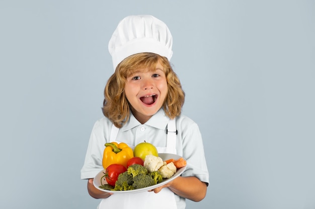 クックキャップとエプロンでフルーツサラダとcを作っている1歳の子供の興奮した面白いシェフの料理人の肖像画