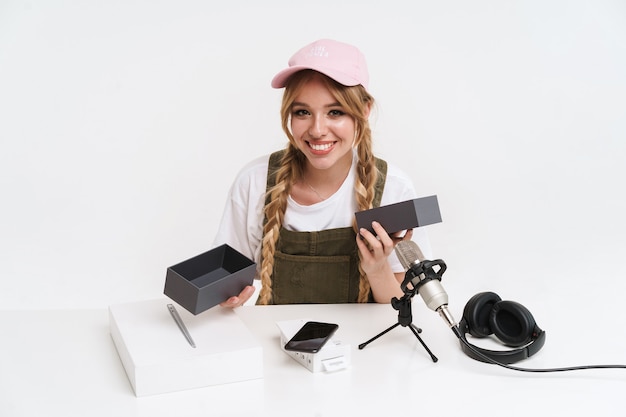 excited girl recording blog broadcast with microphone about new smartphone isolated on white wall