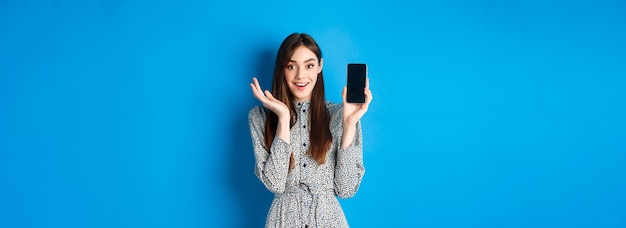 Excited girl showing empty smartphone screen and gasping fascinated demonstrate shopping app standin