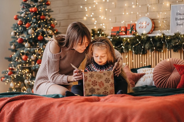 어머니와 함께 흥분한 소녀는 산타 클로스, 행복한 어린 시절, 휴일 축하, 크리스마스 기적의 선물 상자를 엽니 다