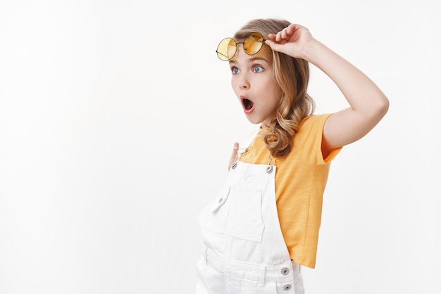 Excited gorgeous glamour young girl, fashionable child checking out incredible offer, take-off glasses look sideways copy space left amazed