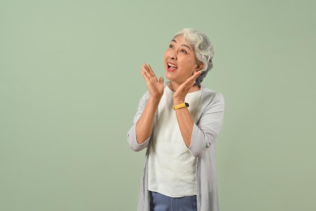 Excited gray haired senior woman posing over green pastel background