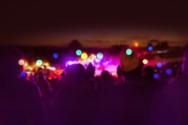 Возбужденные гости впереди на ночном музыкальном фестивале Модный фестиваль размыл текстуру боке в летнюю ночь