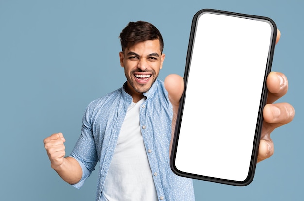 Excited guy shakes clenched fist and showing cell phone mockup