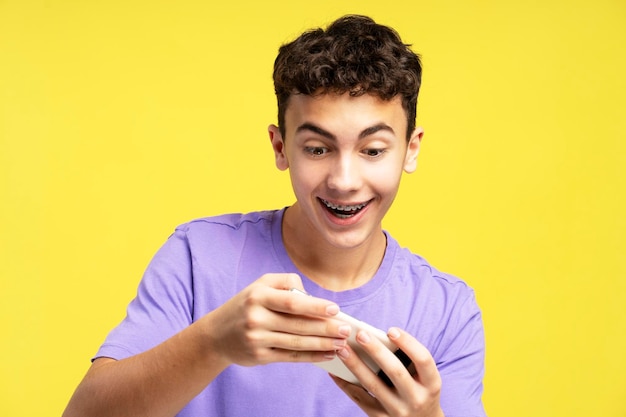 Excited handsome boy teenager holding mobile phone using mobile app playing game