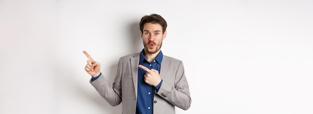 Excited handsome caucasian businessman in suit pointing right at logo say wow and look amazed standi