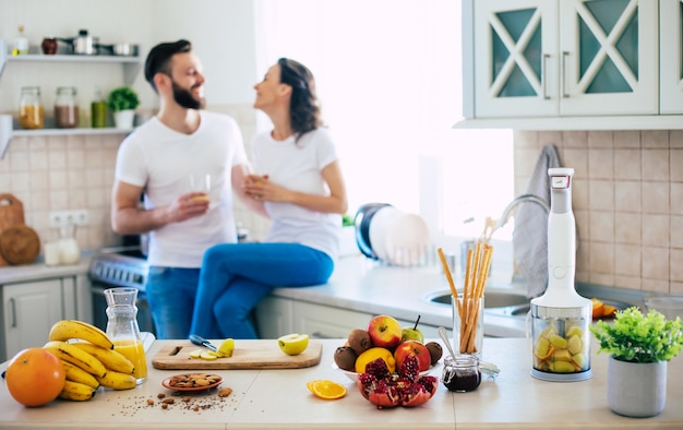 Excited happy beautiful young couple in love cooking in the kitchen and having fun together while making fresh healthy fruits salad