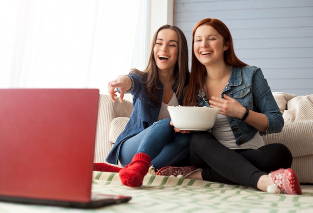 Возбужденные и счастливые красивые молодые друзья смотрят телевизор и едят попкорн