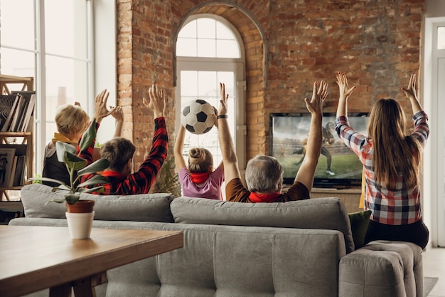 興奮した、幸せな大家族チームが自宅のソファで一緒にスポーツの試合を見る