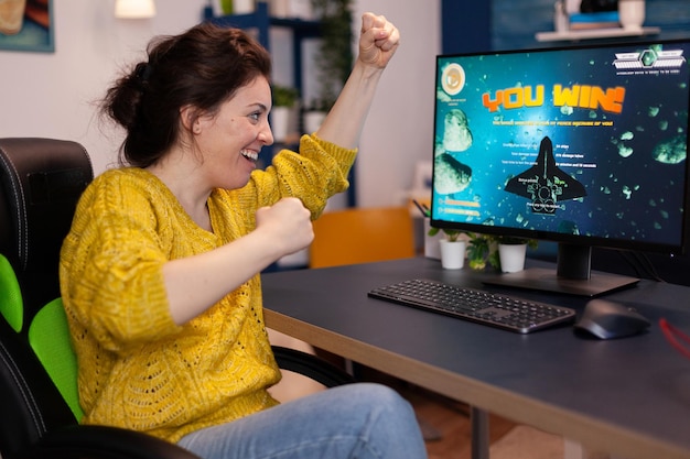 Excited happy competitive gamer woman winning space shooter videogames during online game championship in living room at home. Player performing cybersport tournament. Video game victory