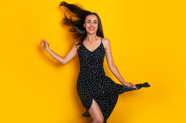 Excited happy cute modern woman in a summer dress is dancing and having fun isolated on yellow background