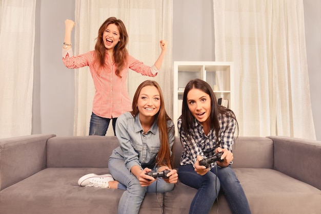 Ragazze felici eccitate che si siedono sul divano e giocano ai videogiochi