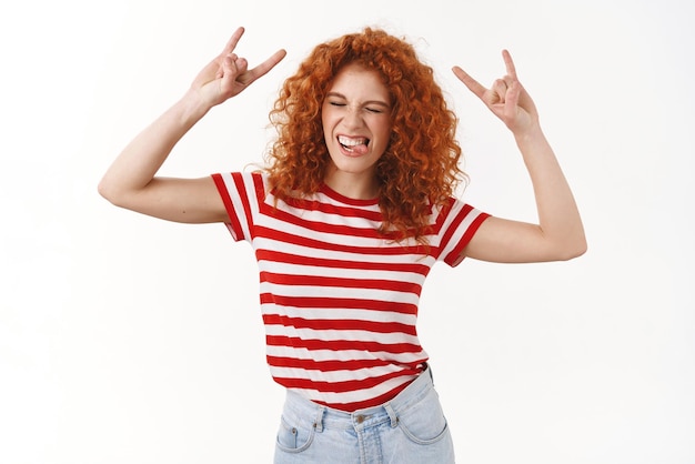 Excited happy lively attractive redhead curlyhaired woman enjoy summer positive vibes awesome music show tongue playful close eyes dancing rocknroll entertained cool concert heavy metal gesture