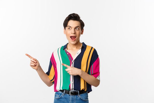 Excited happy man pointing left at promo banner, looking amazed, standing against white