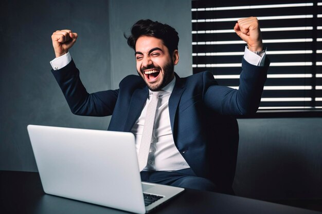 Excited happy man in a suit sitting at the desk with a laptop on it