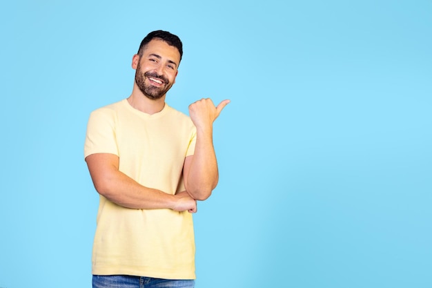 Excited happy positive young arabic man pointing fingers sideways at copy promotional product presen