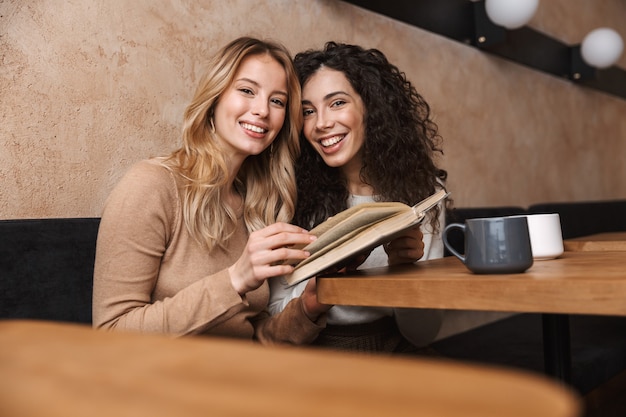 возбужденные счастливые красивые девушки друзья сидят в кафе, пьют кофе и читают книгу