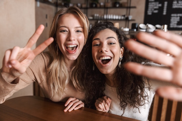 excited happy pretty girls friends sitting in cafe take a selfie by camera