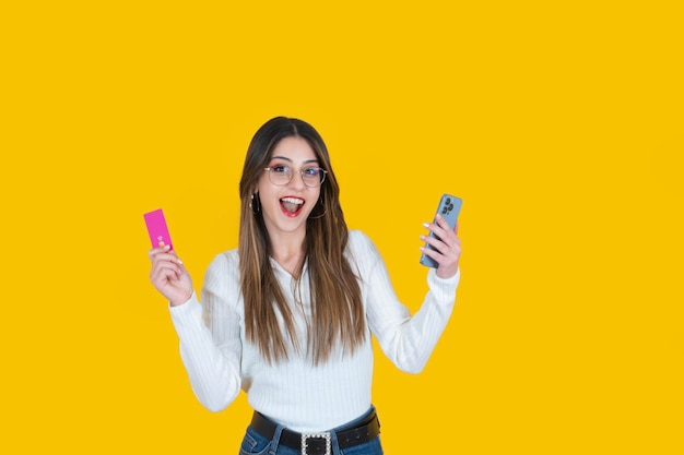 Excited happy woman holding plastic pink credit card and smartphone recommending online shopping