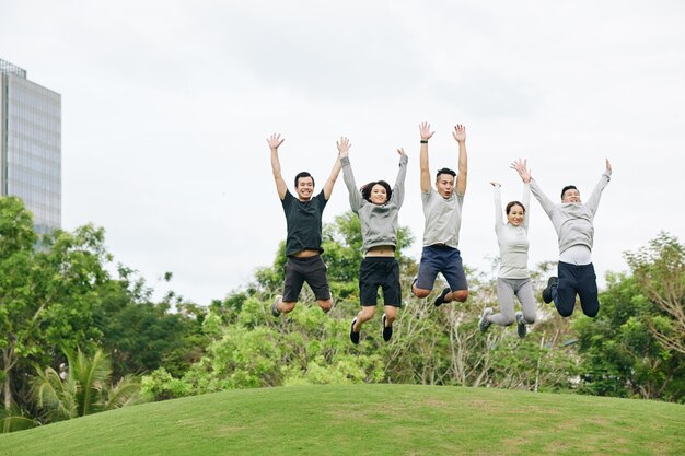 Photo excited happy young vietnamese people jumping in city park after finishing outdoor training