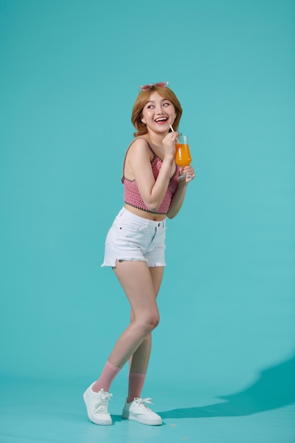 Excited happy young woman enjoys a cool cocktail laughing and having fun isolated on turquoise party summer background