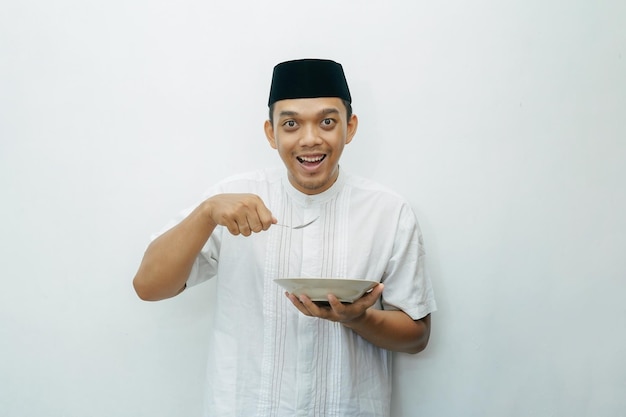 Photo excited indonesian asian muslim man holding spoon and plate on hands ready for eating