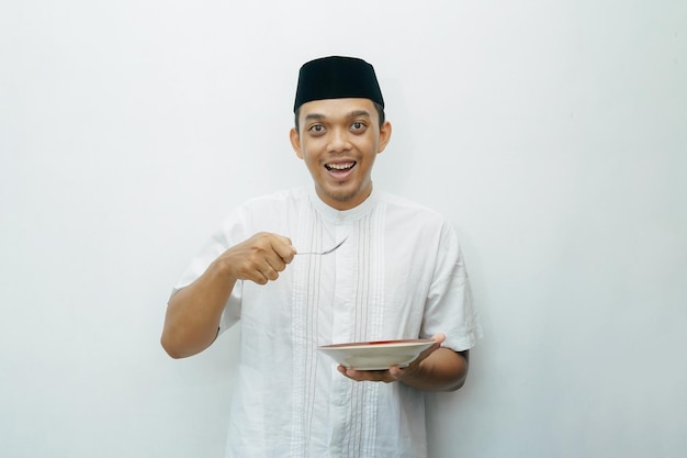 Photo excited indonesian asian muslim man holding spoon and plate on hands ready for eating