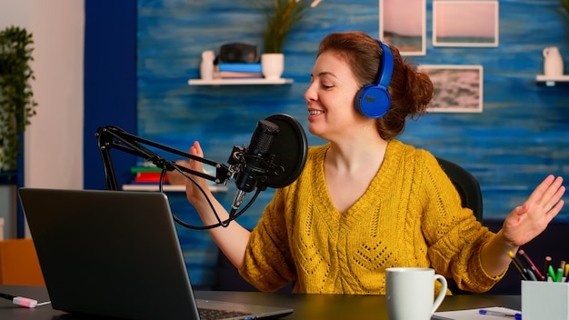 Excited influencer recording vlog in living room studio, making content for podcast talking in microphone