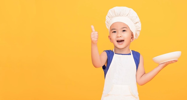 Photo excited kid in chef uniform showing thumbs up on yellow background