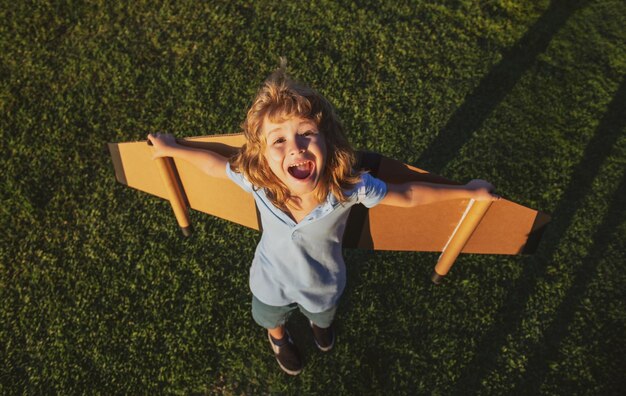 Excited kid with backpack wings child playing pilot aviator and dreams outdoors in park smiling kid