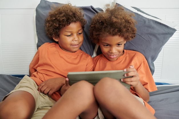 Excited kids sitting on bed and playing game on tablet computer